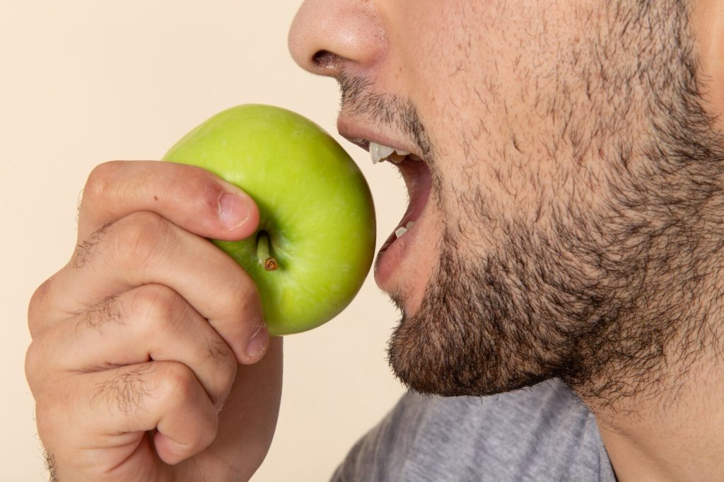 Young man biting green apple confidently with Dental Implants