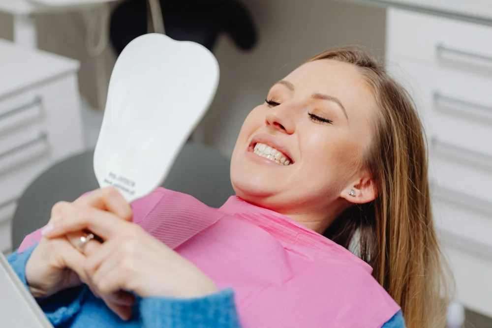 Happy female patient looking in a mirror at her successful single tooth implant results
