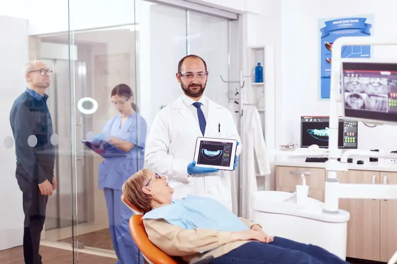 A dentist stands beside a patient, holding a tablet that shows digital scans of teeth during a dental implant consultation at DENTAL IMPLANT PROFESSIONALS in Sydney.